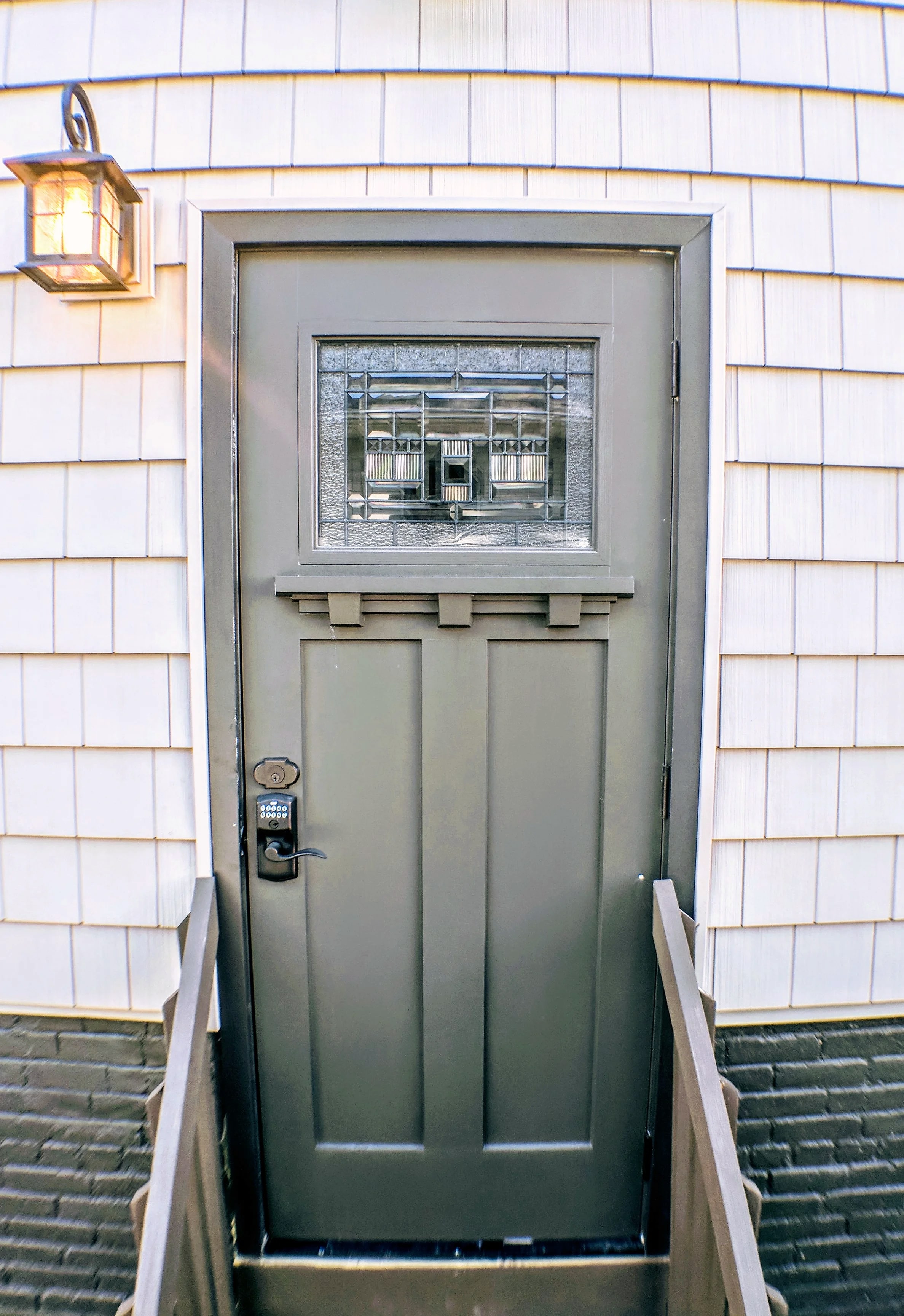 Gray craftsman-style door with leaded glass on shingled wall