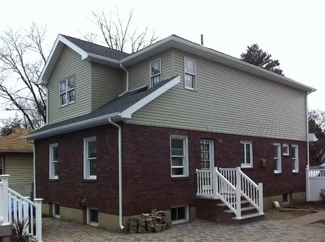Brick and green vinyl siding house with new roof and white railings